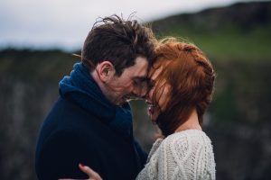 adventurous couple nuzzling on a windy cliffside in northern ireland