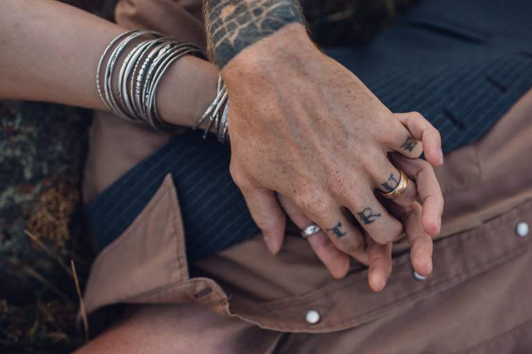 intimate couple with jewelry and tattoos holds hands during their anniversary adventure session