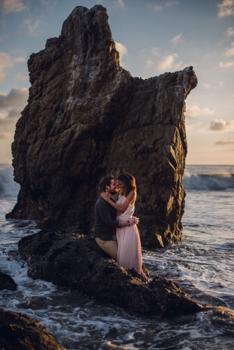 adventurous couple embracing on a rock in the ocean