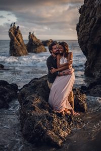 adventurous couple embracing on a rock in the ocean