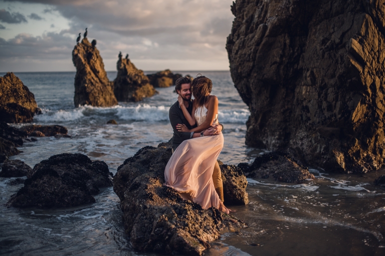 adventurous couple embracing on a rock in the ocean