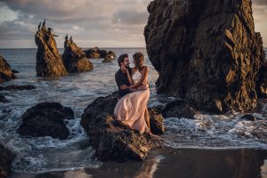 adventurous couple embracing on a rock in the ocean