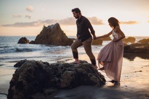 adventurous couple climbing on a rock at the beach