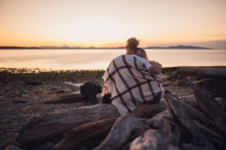 adventurous couple embracing on driftwood beach at sunrise