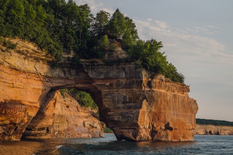 orange rock formations in the water covered with trees along the Pictured Rocks shoreline in the upper peninsula Michigan at sunset