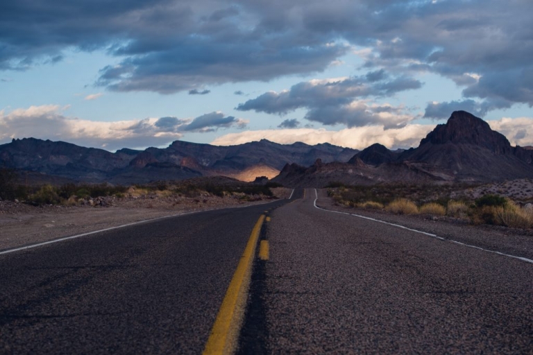 A long desert road leading towards the mountains with a sunset glow in the distance and blue clouds overhead in Oatman, Arizona