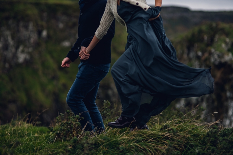 adventurous couple running along a grassy hillside in northern ireland