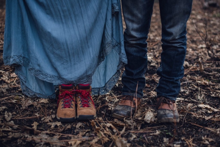 Up close detail of a man and woman's hiking boots as they stand in a forest