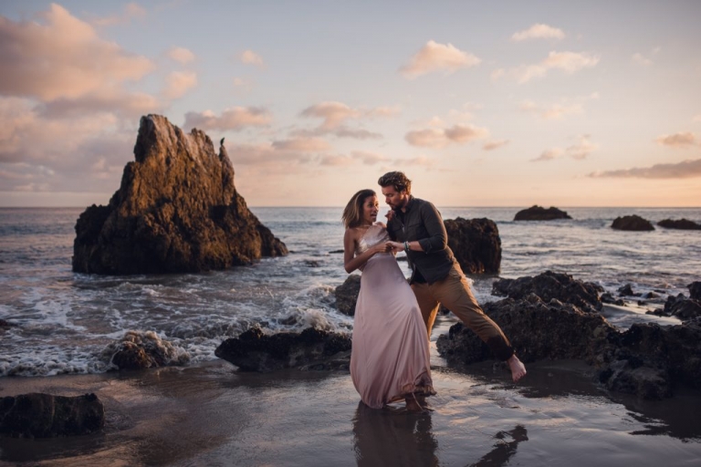 Couple stumbles as they dance among the rock formations on El Matador Beach and the man steadies the woman wearing a long pink gown