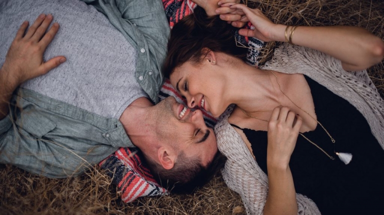 Dark haired couple lies on the ground smiling face to face during their engagement session in solstice canyon California 