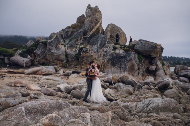 Couple shares a kiss during their elopement on a rocky shoreline in Big Sur