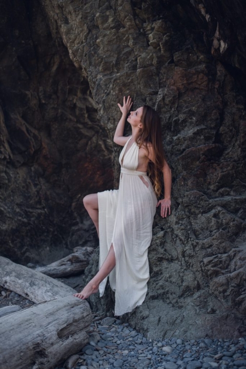 woman in a white dress reclining on rocks on ruby beach in washington