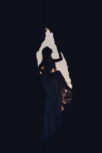 silhouette of a woman with long hair sitting in a hole in the rock