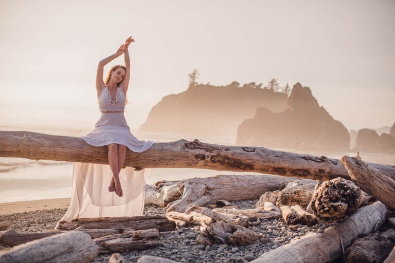 red head bride sitting on a driftwood tree stretching towards the sky at sunset on ruby beach