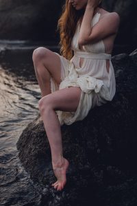 red head woman sitting on a rock next to the water on ruby beach just after sunset