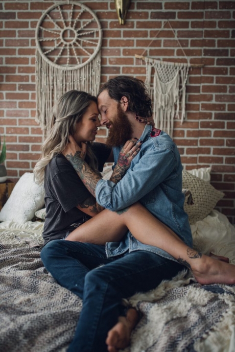 bohemian couple sitting on their bed smiling and embracing during their at home snuggle session