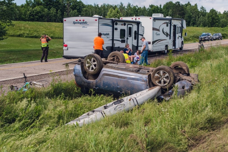 blue rav4 flipped upside down in a grassy ditch at the scene of a car accident with two rvs in the background