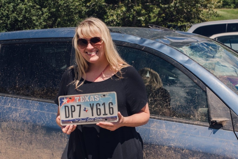 blonde woman with a seatbelt scar holds up the texas license plate from her totaled toyota rav4 after surviving a terrible accident 